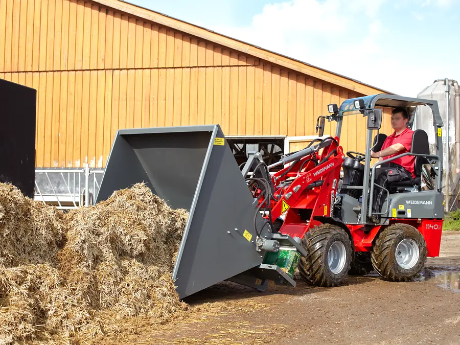 Compacte hoflader met bak aan het werk op een erf